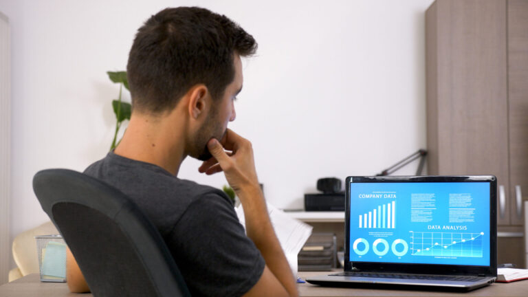 Um homem senta-se em uma mesa, olhando atentamente para uma tela de laptop que exibe gráficos e diagramas rotulados como Dados da empresa e Análise de dados em um ambiente de escritório moderno, usando software para lotéricas para agilizar os insights de negócios.
