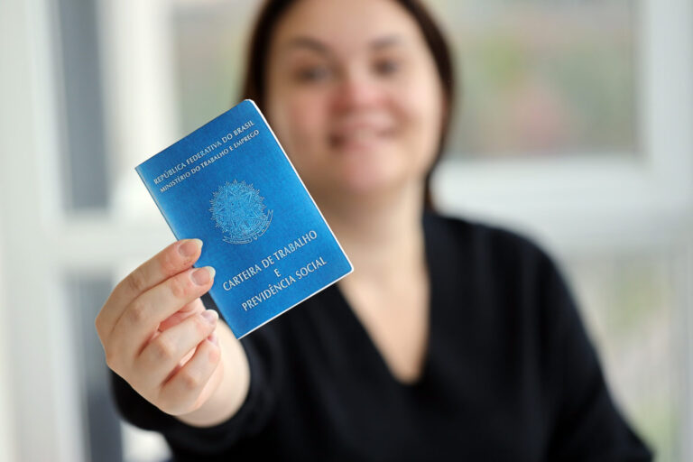 Uma pessoa com traços faciais borrados segura uma Carteira de Trabalho e Previdência Social brasileira azul, destacando a importância de um software para lotéricas no gerenciamento moderno da força de trabalho.