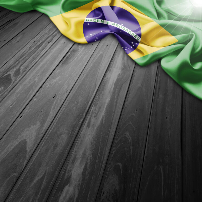Uma bandeira brasileira enrolada na borda superior de uma superfície de madeira escura, com a luz do sol brilhando no canto superior direito da bandeira, evoca a cultura vibrante na qual o jogo do bicho se tornou a maior tradição popular.
