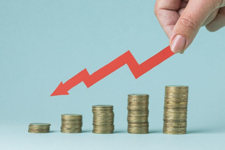 Uma mão segura uma seta vermelha em ziguezague apontando para cima, acima de pilhas crescentes de moedas, simbolizando o crescimento financeiro enquanto o governo aposta em medidas para reverter o corte no orçamento, contra um fundo azul claro.