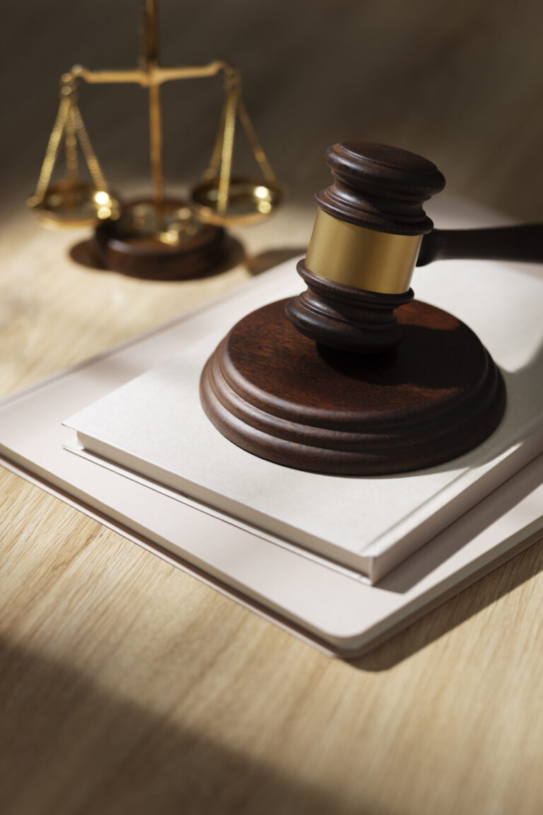 Um martelo de juiz de madeira repousa sobre um livro fechado em cima de um laptop, com uma balança de justiça de bronze ao fundo em uma mesa de madeira - preparando o cenário para discussões como o road show para concessão da Lotex.