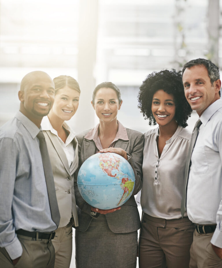 Cinco pessoas vestidas profissionalmente estão juntas, sorrindo para a câmera. A pessoa no centro segura um globo, sugerindo um tema de trabalho em equipe e diversidade no local de trabalho, como quando um grupo propõe criar tribunal para julgar convenções em escala global.