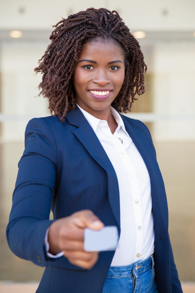 Uma mulher de blazer azul-marinho e camisa branca sorri enquanto estende um cartão em branco para a câmera, como se estivesse perguntando se os apostadores de loterias podem ser obrigados a apresentar identificação. O fundo está claro e fora de foco.