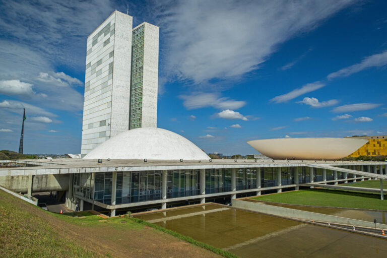 A imagem mostra o edifício modernista do Congresso Nacional em Brasília, Brasil - onde o Senado também aprovou a legalização das apostas - com uma torre retangular alta e duas cúpulas sob um céu azul brilhante.