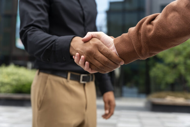Duas pessoas estão se cumprimentando ao ar livre, em frente a um prédio de vidro, representando unidade e colaboração - um exemplo do por que defender o movimento sindical para promover a solidariedade no local de trabalho.