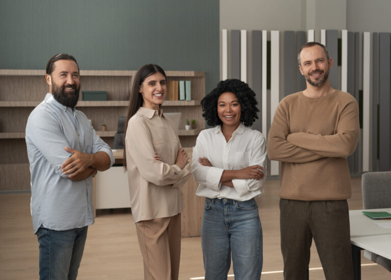 Quatro pessoas estão em um escritório, sorrindo e de braços cruzados, refletindo uma vibração amigável e profissional. Seu trabalho em equipe incorpora o endomarketing: conceitos e aplicação, com estantes de livros visíveis ao fundo.