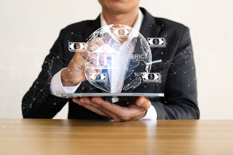 Uma pessoa de terno segura um tablet, com um holograma de globo digital exibindo símbolos do BRICS e do dólar, representando finanças globais, tecnologia e venda recorrente - entenda como esses fatores impulsionam o mercado global.