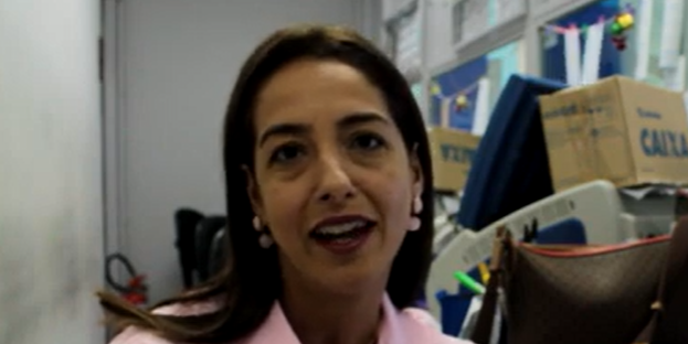 Uma mulher com longos cabelos castanhos, usando um top rosa e brincos, está dentro de casa perto de caixas de papelão e itens diversos - talvez comemorando Casos de Sucesso no Loteamento Capela de Santana.